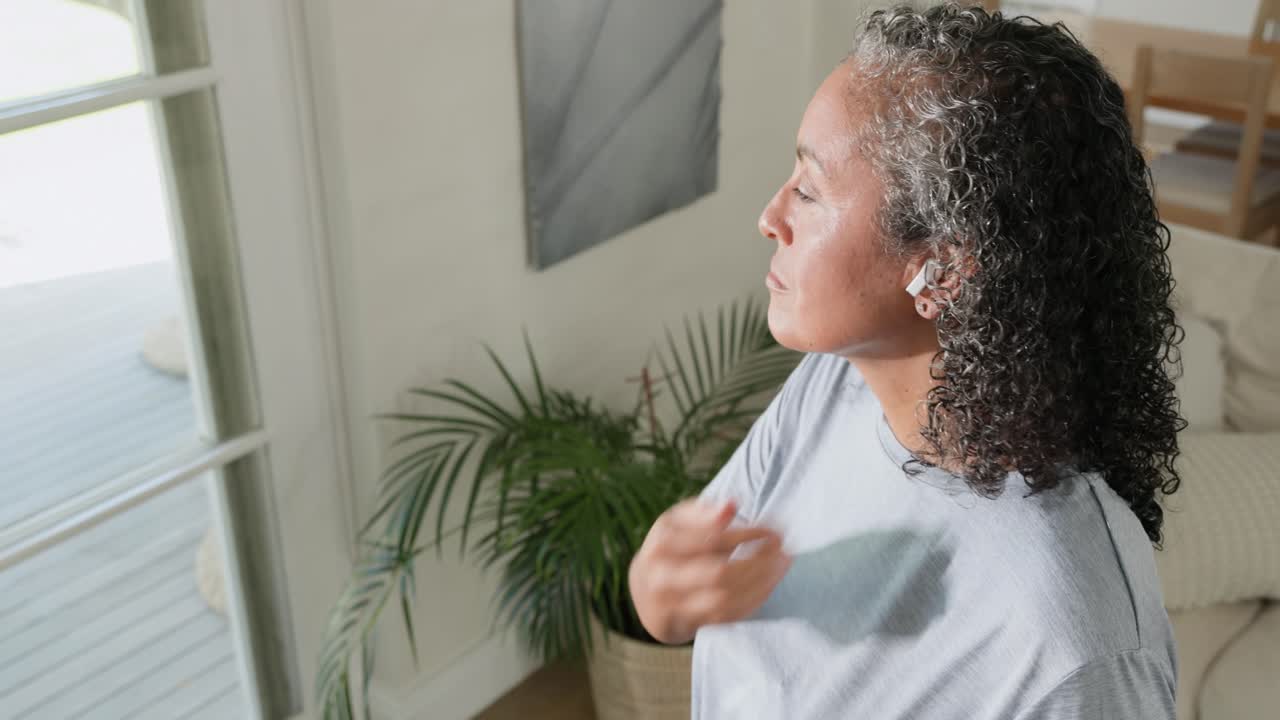 African American woman looking out door, inserting earbuds, tapping smartwatch preparing workout