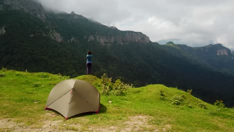 360 degree shot a traveler tourist girl stands by road camping tent in beautiful landscape of highland hills green meadow, high mountain above pine forest aerial summer georgia borjomi national park