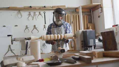 African-american-male-carpenter-wearing-protective-helmet-turning-wood-on-a-lathe-at-carpentry-shop