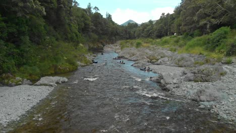 people paddle kayak down the rapid with rock boulders on beautiful pristine clear blue pelours river, new zealand - aerial drone