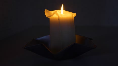 Slow-moving-shot-around-a-lit-candle-in-a-dark-room-in-full-frame