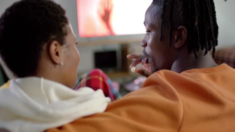 African-american-couple-relaxing-watching-tv-and-eating-popcorn-at-home,-slow-motion