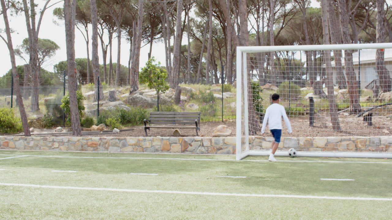 Boy playing soccer on field, dribbling ball near goal in park, copy space