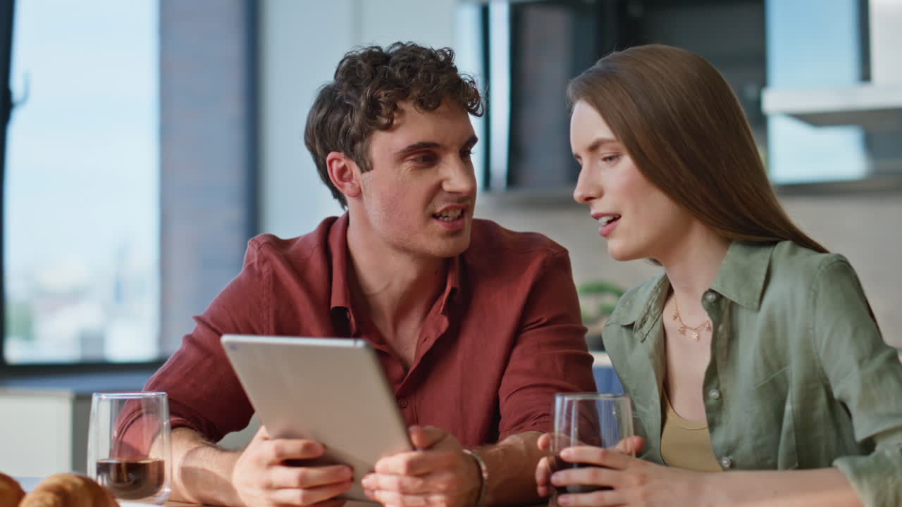 Spouses discussing online purchase at tablet sitting apartment kitchen closeup