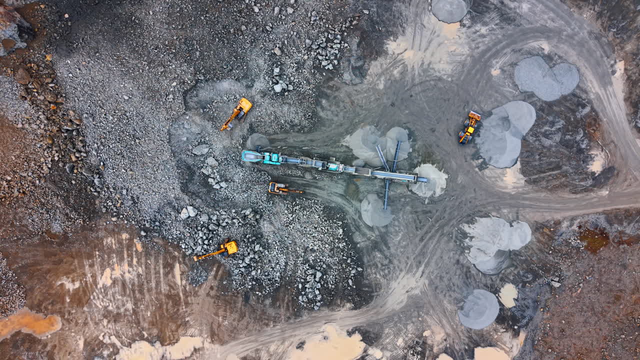 Overhead drone shot of mobile stone crushing machinery in pit. Top down perspective of stone processing equipment and excavators on a rocky quarry floor