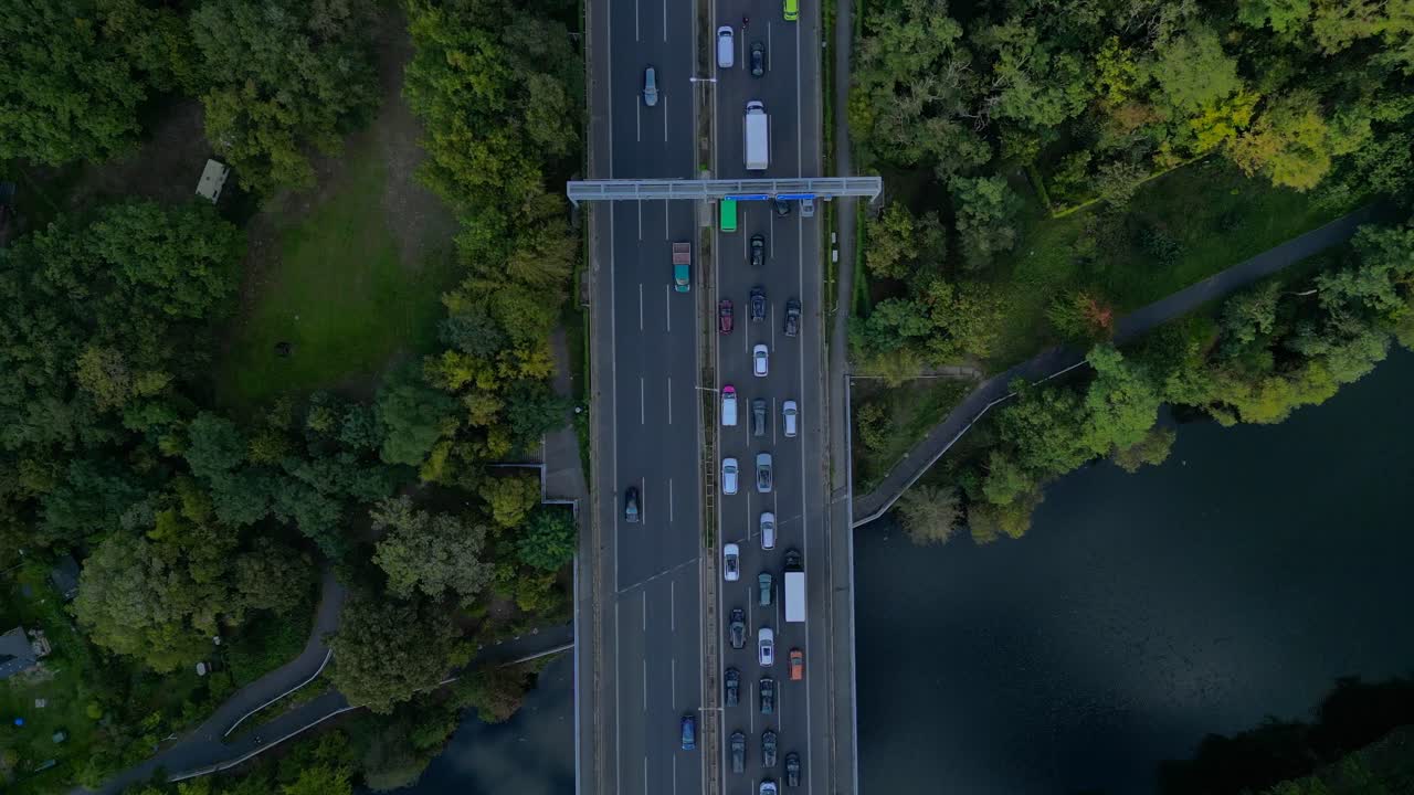 busy highway traffic crossing a bridge over a river surrounded by trees. Majestic aerial view flight vertical bird's eye view drone