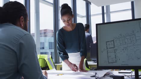 Two-diverse-male-and-female-colleagues-looking-at-architectural-blueprints-on-desk-and-talking