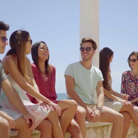 Young-friends-sitting-on-stone-wall-near-beach