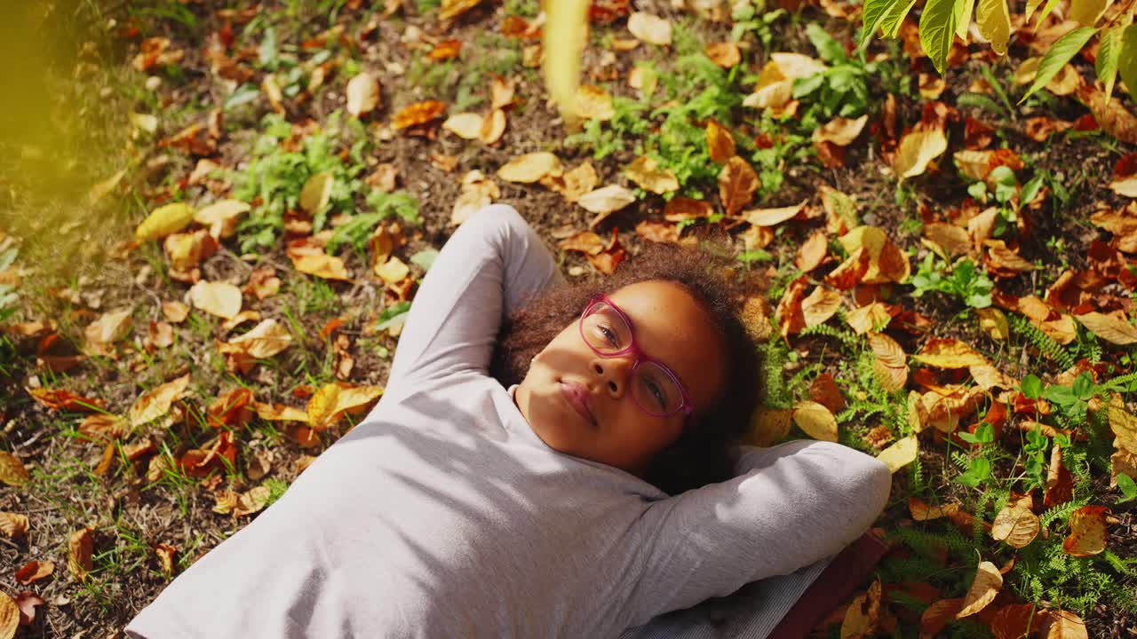 Giovane ragazza con gli occhiali sdraiata sulle foglie autunnali in un parco