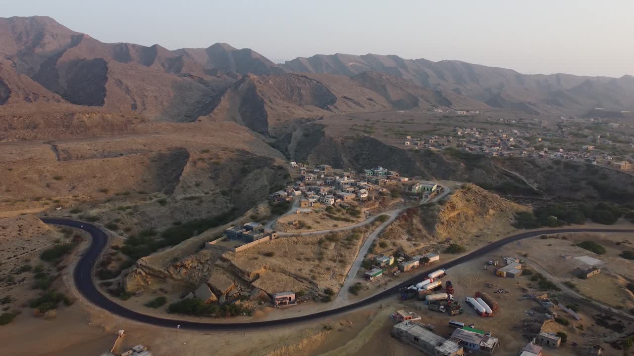 Una bellissima autostrada sinuosa circondata da piccoli villaggi e dalla catena montuosa del Parco Nazionale Ormara Hingol sullo sfondo, in Balochistan