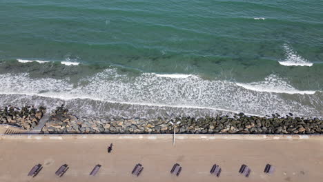 aerial shot of couple walking along shoreline with picnic benches located lower part of footage