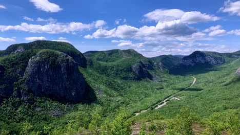 Lushes-green-rocky-mountainous-valley-panning-left-to-right-on-a-blue-but-partly-cloudy-day