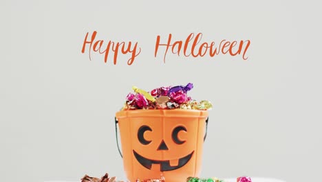 Animation-of-halloween-text-over-carved-pumpkin-bucket-with-sweets-on-grey-background