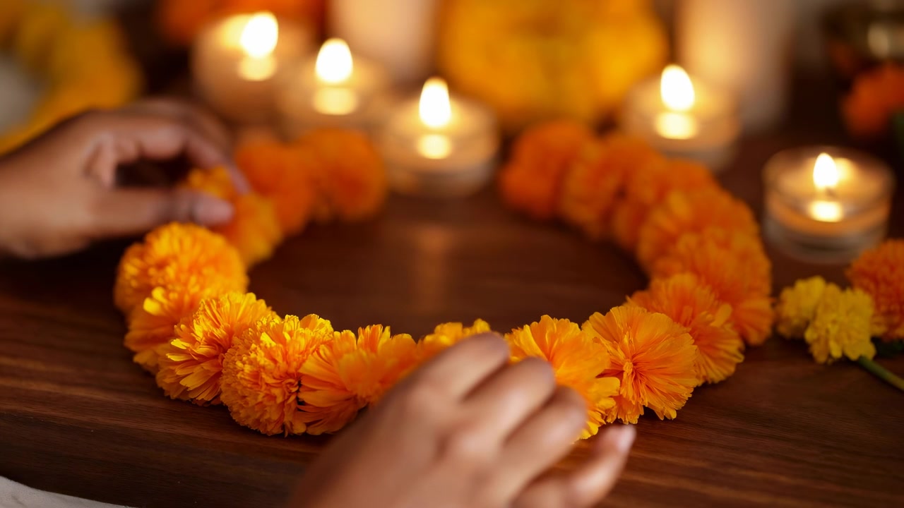 Close view shows hands adjusting bright marigold blossoms around ring arrangement on dark wood table with glowing candles in background, highlighting texture, color, and careful floral placement.