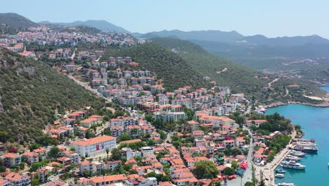 Amplio-Dron-Aéreo-De-Edificios-Europeos-Con-Techos-Naranjas-En-Una-Gran-Colina-Costera-Y-Barcos-Atracados-En-El-Puerto-Deportivo-De-Kas-Turquía-En-Un-Día-Soleado-De-Verano