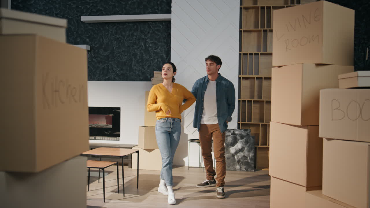 Couple watching new house living room full boxes. Family discussing interior