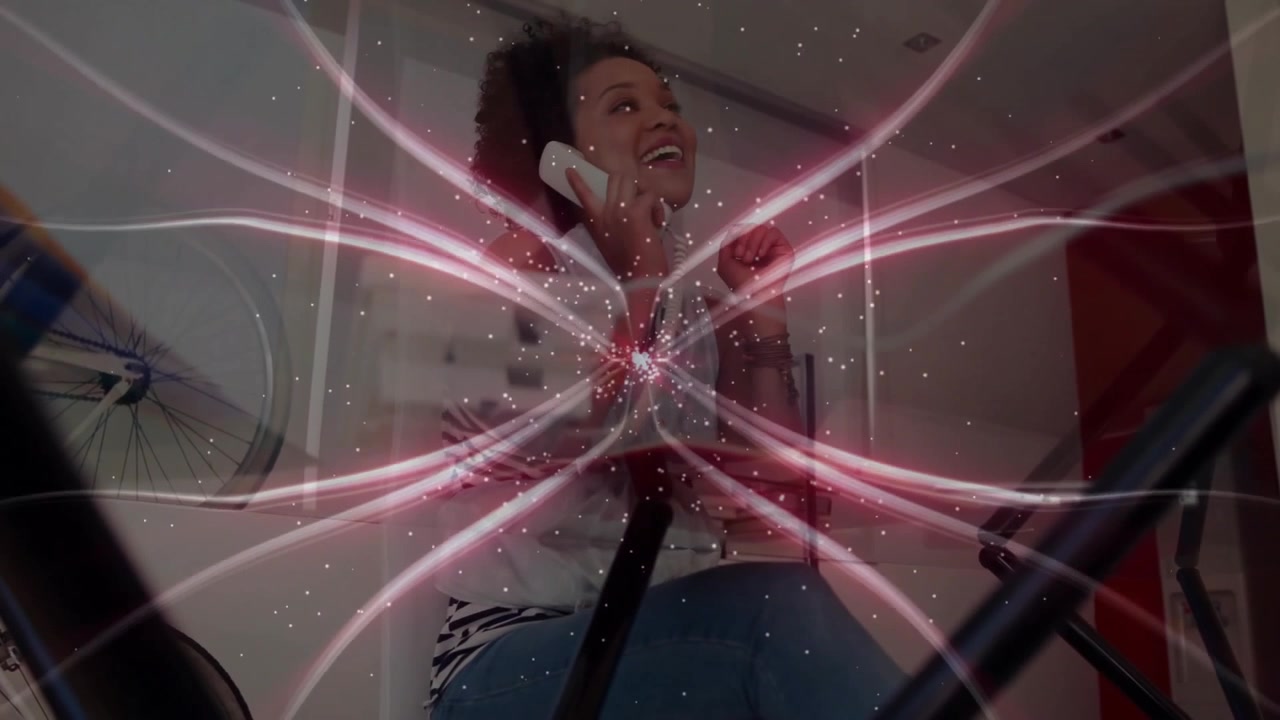 Mujer sosteniendo el auricular del teléfono escuchando una llamada en casa, creando un efecto tecnológico de explosión estelar rosa pulsante.