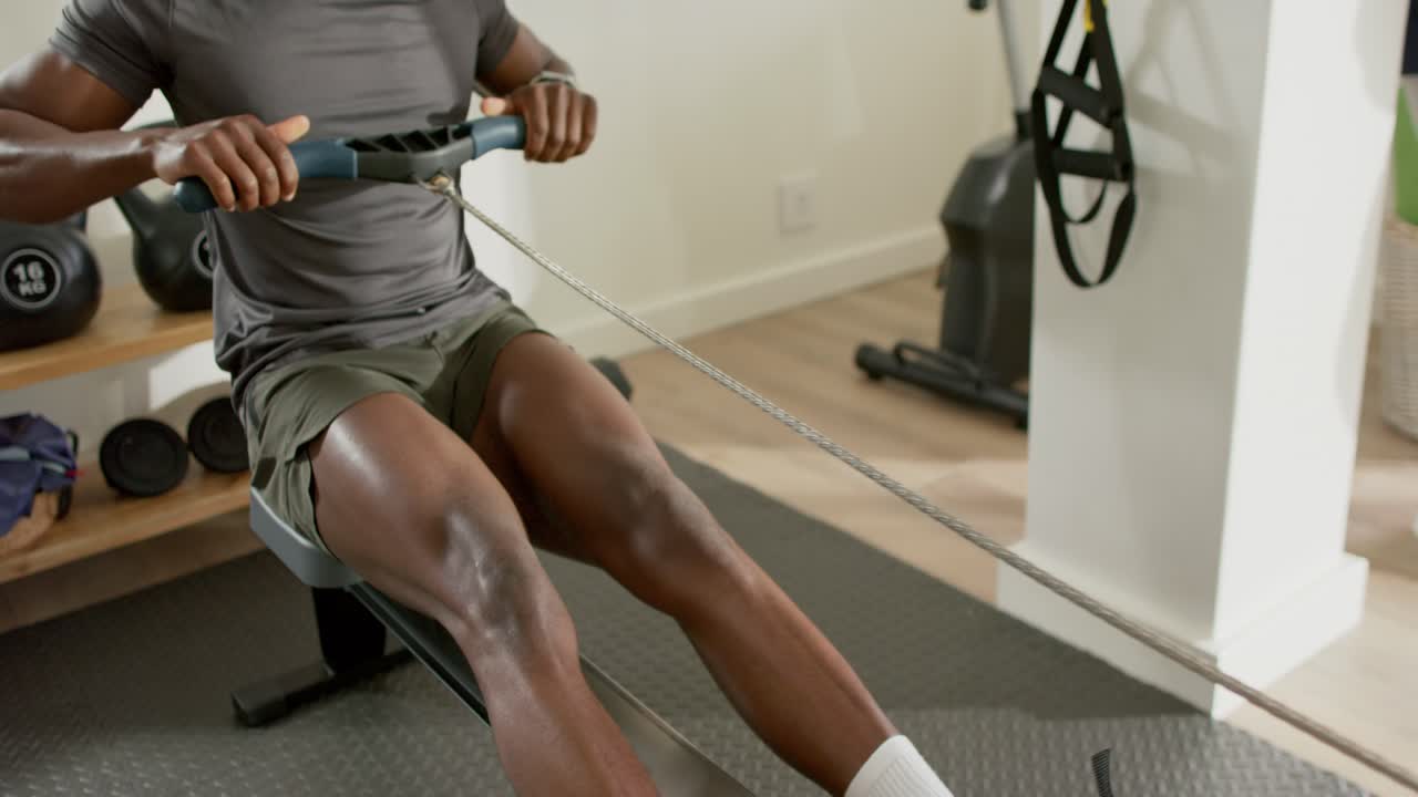 At start, man is bending knees and sliding seat for recovery on rowing machine for fitness