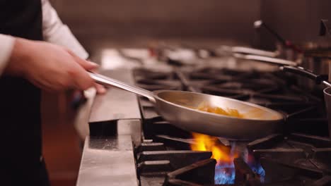 cook shakes the silver pan with pasta back and forth while the pasta cooks on the fire