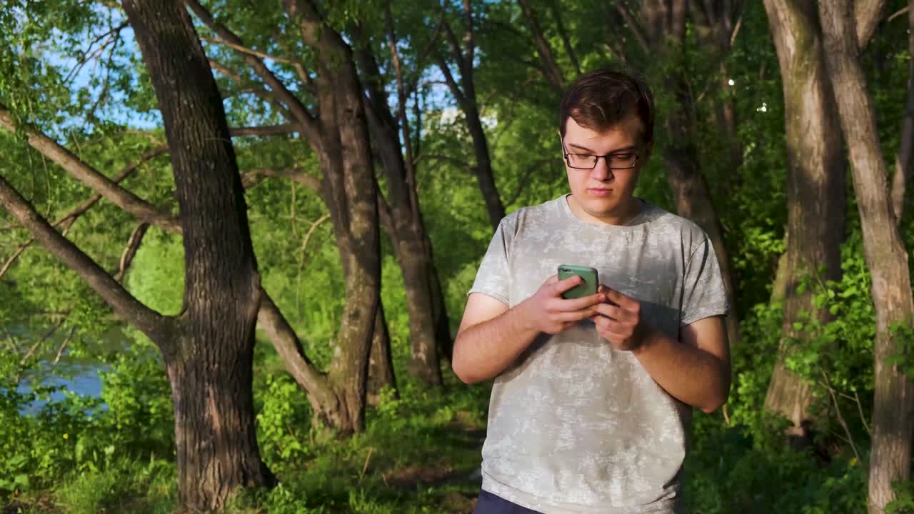 강 근처의 숲에서 스마트폰을 사용하는 젊은 남자