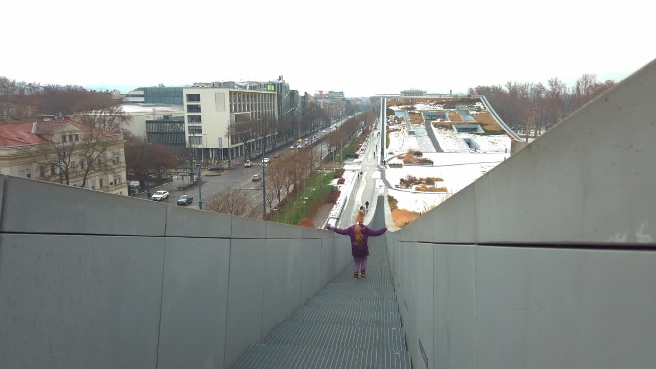 Inquadratura in movimento cinematografica di un bambino che scende scale architettoniche a Budapest. Design moderno di parco urbano a Varosliget con vista sulla città durante una giornata luminosa in un video clip professionale in 4K.