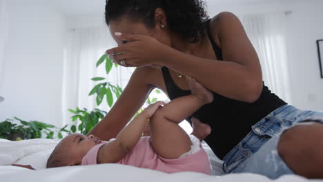 loving mother playing game of peekaboo with baby daughter lying on bed at home