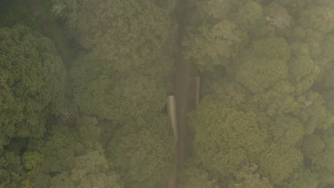 Aerial-following-shot-of-a-commuter-train-moves-on-the-forest-at-foggy