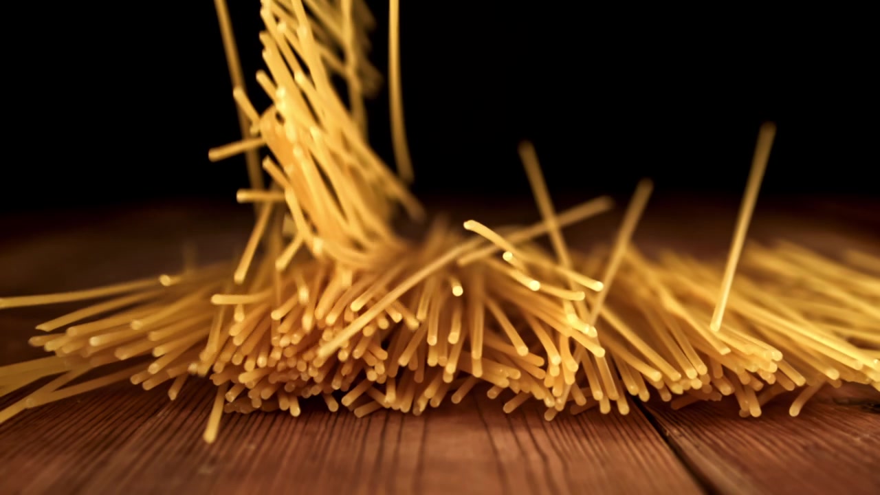 Spaghetti crudi che cadono al rallentatore su un tavolo di legno