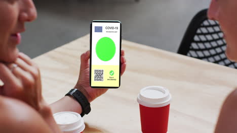 hombre en un café mostrando un teléfono inteligente con certificado de vacunación contra la covid, bandera de la ue y código qr en la pantalla