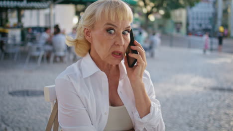 angry senior woman talking cellphone in city cafe close up. rich pensioner call