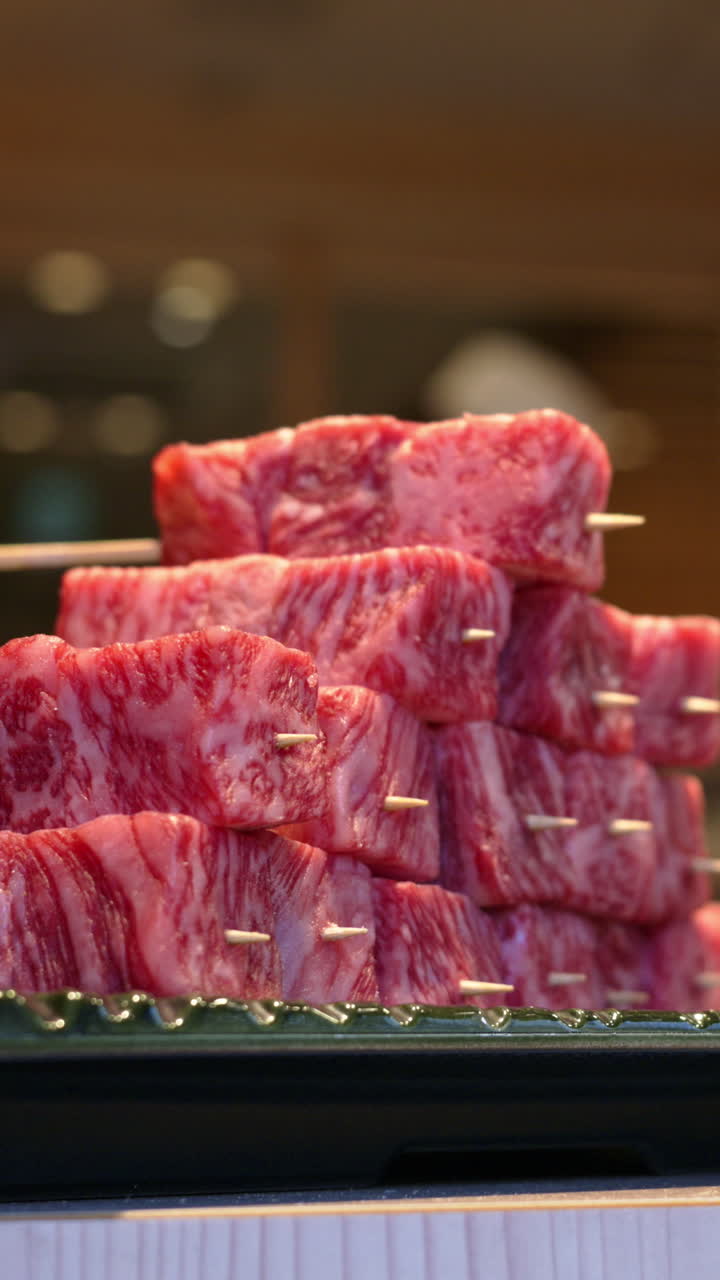 Close up of multiple pieces of Wagyu beef with a chef cooking in the background at the Tsukiji Fish Market in Japan. Vertical