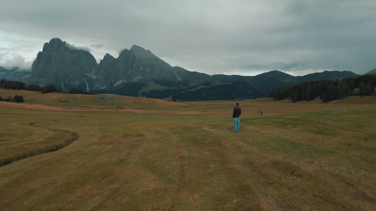 Tourist enjoying the landscape of Alpe di Siusi in Dolomites, Italy, walking on a meadow with Sassolungo mountain in the background