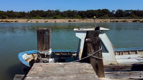 an old wooden pier with a vintage and grungy fishing boat tied to it - low altitude flyover or push in towards the river