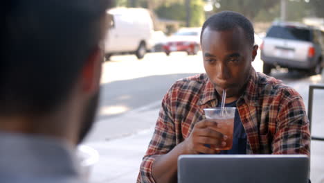 two male friends with cold drinks and laptop outside coffee shop