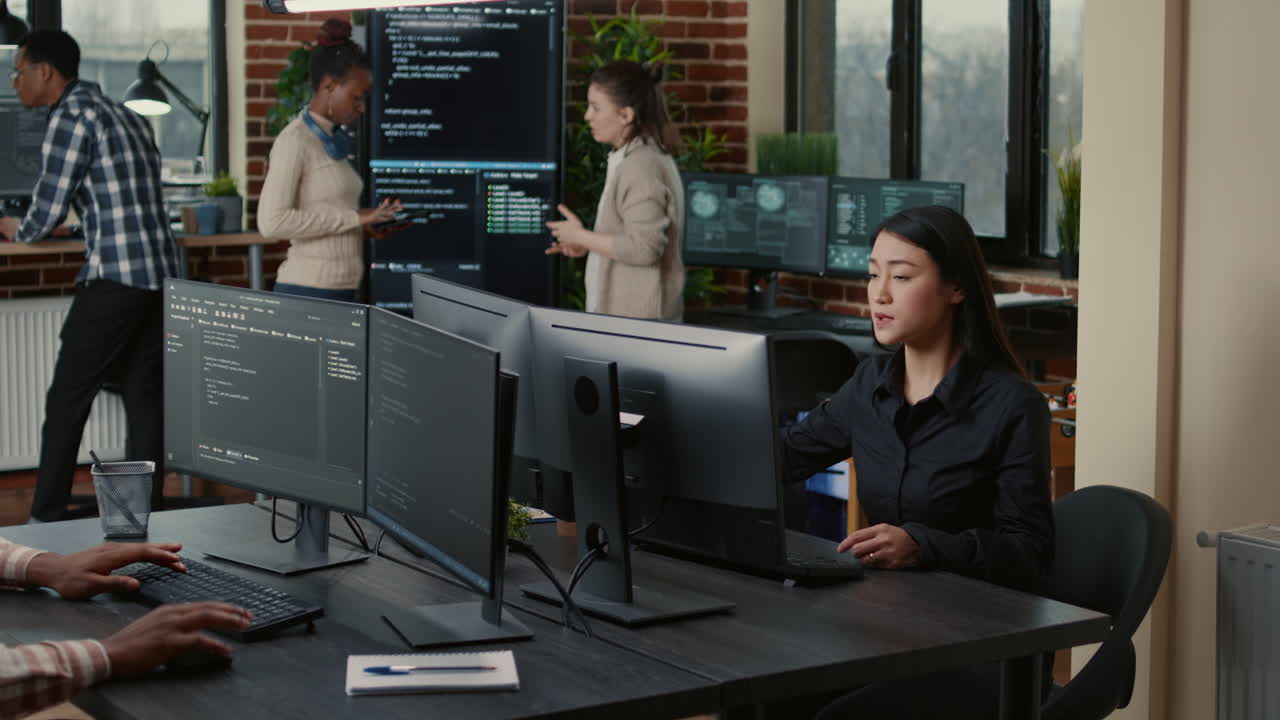 Programer with clipboard sitting down at desk in front of programer writing code