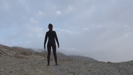 long shot of a mysterious woman in black standing in the desert with the cloudy sky at sunrise