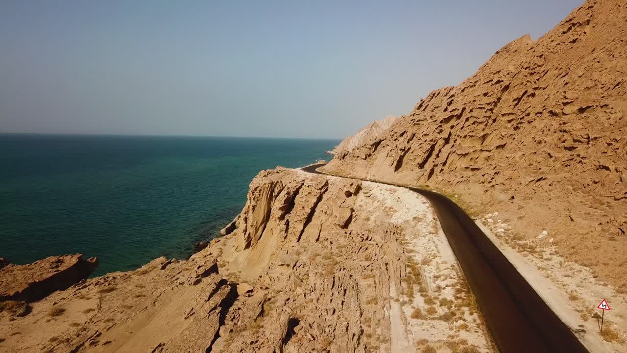 Asphalt road alongside the beach wind erosion rock solid mountain cliff seaside beach coastal landscape of ocean in left mountain in right wonderful road trip concept of travel summer vacation iran