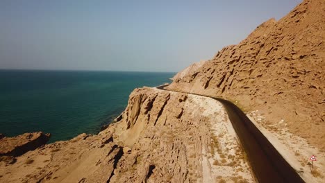 Carretera-Asfaltada-A-Lo-Largo-De-La-Playa-Erosión-Eólica-Roca-Sólida-Montaña-Acantilado-Playa-Costera-Paisaje-Costero-Del-Océano-En-La-Izquierda-Montaña-En-La-Derecha-Maravilloso-Viaje-Por-Carretera-Concepto-De-Viaje-Vacaciones-De-Verano-Irán