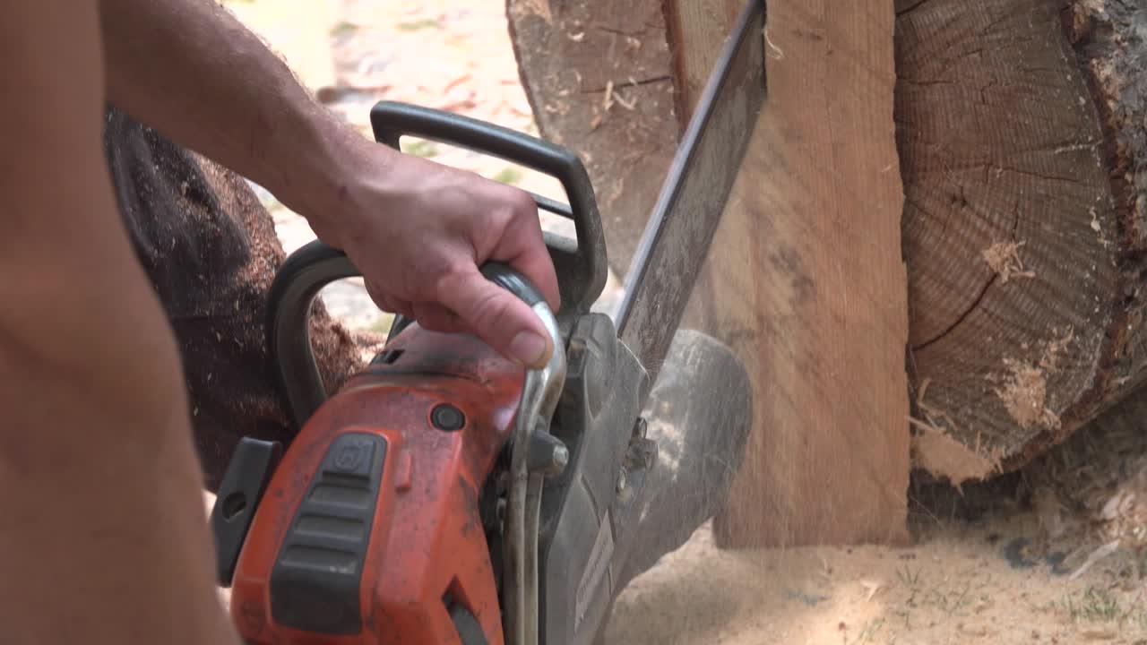 Homem usando uma motosserra para rachar um pedaço de madeira, firmando a peça com sua bota de trabalho.