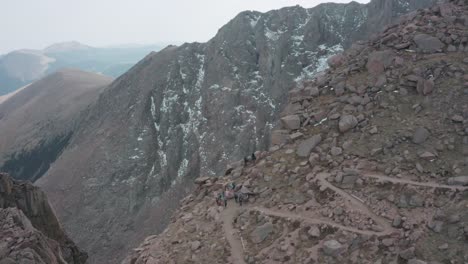 Aerial-descent-reveal-of-hikers-on-cliff-precipice