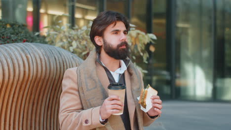 indian young businessman tourist enjoy lunch break eating sandwich and drinking hot coffee or tea