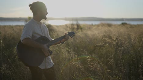 man playing guitar in a field at sunset