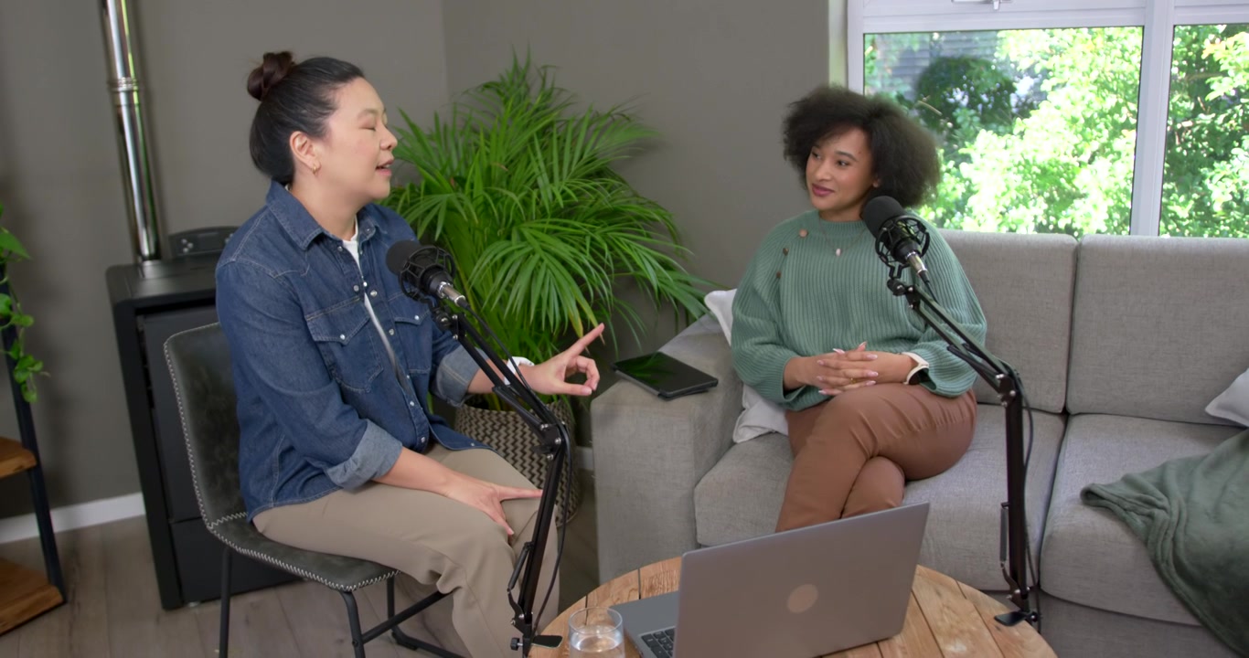Donna asiatica e donna afroamericana che registrano, mentre la donna a sinistra dà il via, gesticolando verso i microfoni.