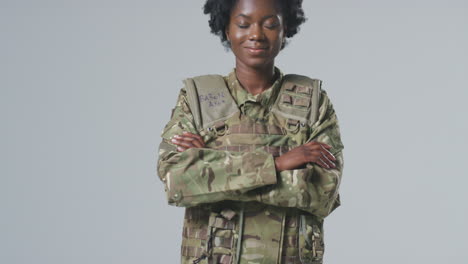 full length studio portrait of smiling young female soldier in military uniform on plain background