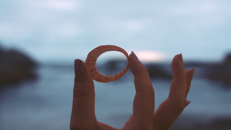 hand holding a ring over the ocean sunset