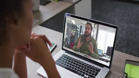 mid section of african american woman having a video call with male colleague on laptop at office