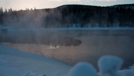 dreamy frosty morning mist rising from cold alpine woodland frozen lake at sunrise, sweden