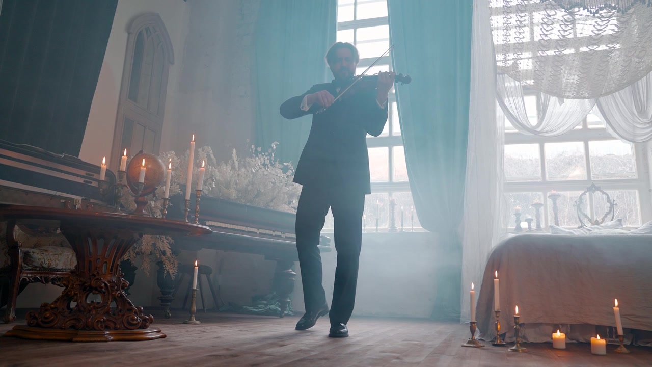 Klassisk musiker spelar fiol i ett dimmigt rum upplyst av levande ljus.