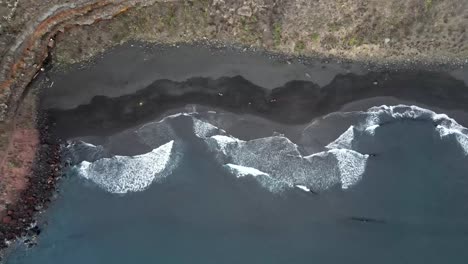 aerial drone view of ocean waves washing black sand beach on canary islands, spain