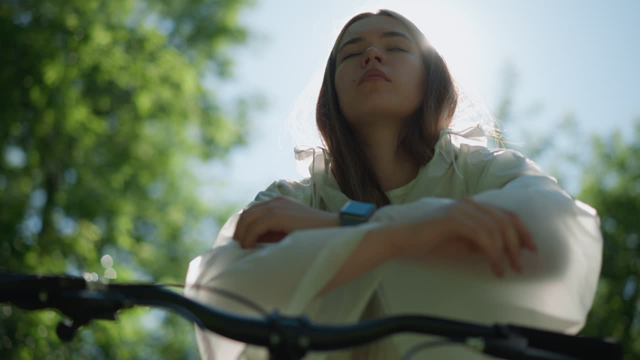 반투명한 레인코트를 입은 여성이 밝은 빛에서 후드를 내려 놓고, 그녀의 상하는 얼굴 주변에 부드럽고 에테리얼한 빛을 만들어, 배경에는 흐릿한 초록색이 있습니다.